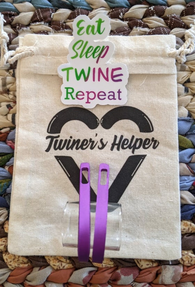 May include: A white canvas bag with the text "Twiner's Helper" and a heart shape. The bag has a sticker that says "Eat Sleep Twine Repeat". Two purple twine tools are in front of the bag.
