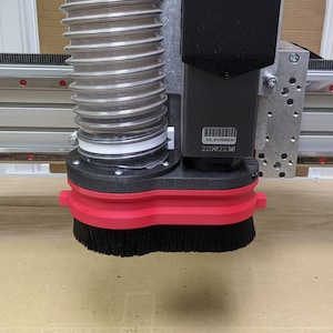 May include: A close-up of a black and red dust collection system with a black brush attached to a CNC machine. The system has a clear hose and a label with the text "TL 41000000 220822318".