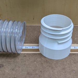 Puede incluir: Un adaptador de recolección de polvo de plástico blanco con un diseño acanalado, junto a una manguera de recolección de polvo de plástico transparente.