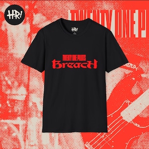 May include: Black t-shirt featuring the red text "TWENTY ONE PILOTS Breach". The shirt has a crew neck and short sleeves. The background is red with a halftone pattern and the words "TWENTY ONE" in white.
