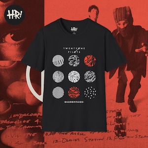 Puede incluir: Camiseta negra de Twenty One Pilots con el nombre de la banda y el título del álbum "Blurryface". El diseño incluye nueve gráficos circulares en negro, blanco y rojo. El logotipo HR! es visible en la parte superior izquierda y central.