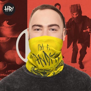 May include: A yellow neck gaiter with black text reading "I'M A THINK" worn by a person. The background is red with a white design and a person in a black outfit. A black and white logo is in the upper left corner.