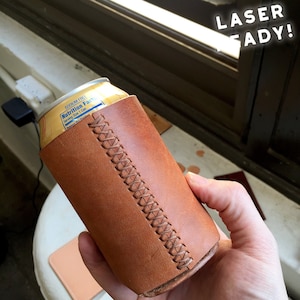 Könnte beinhalten: Ein brauner Getränkedosenkühler aus Leder mit einem genähten Muster. Der Kühler hält eine gelbe Dose mit einem Nährwertetikett. Der Text "LASER READY!" ist im Hintergrund zu sehen.