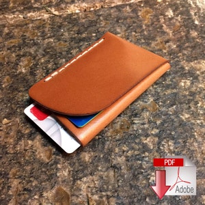 May include: A handcrafted, brown leather cardholder with white stitching along the top edge. The wallet is open, revealing two credit cards. The leather has a smooth finish. The cardholder is designed to hold credit cards and other small items.