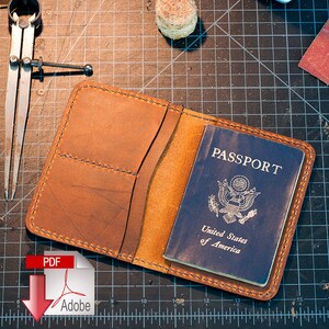May include: Open brown leather passport holder with a blue passport inside. The passport is from the United States of America. The holder has two pockets and is stitched with blue thread. The background is a dark surface with tools.