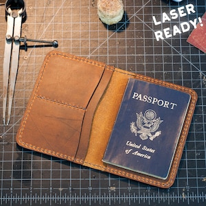 May include: A brown leather passport holder with a blue passport inside. The passport is from the United States of America. The holder is on a black cutting mat. The text "LASER READY!" is in the top right corner.