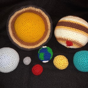 May include: Crocheted planets of the solar system, including the sun, Jupiter, Earth, Saturn, and Neptune. The planets are made with different colored yarn and are all about the same size.