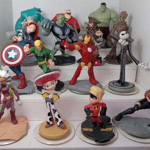 May include: A collection of 12 action figures from various Disney and Marvel franchises, including characters like Iron Man, Captain America, Thor, Woody, and Jack Skellington. The figures are displayed on circular bases with a variety of poses and expressions.