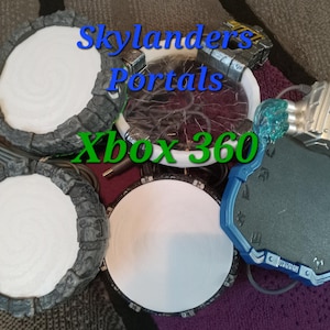 May include: Four Skylanders Portals for Xbox 360. Two are gray and white with a circular platform. One is blue with a circular platform and a silver and blue figure on top. The last one is a gray and white circular platform.