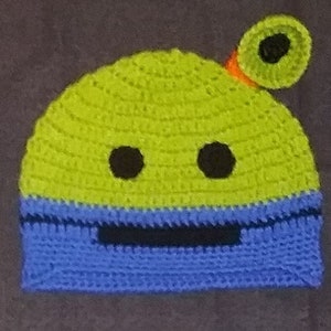 May include: Green and blue crocheted hat with a black eye and mouth, and a green antenna with a black circle on top.
