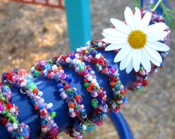 May include: A close-up of a blue metal pipe wrapped with colorful beaded bracelets. A white daisy with a yellow center is nestled in the bracelets.