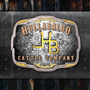 May include: A decorative metal sign with the text "HULLABALOO CATTLE COMPANY". The sign has a silver and gold color scheme with an ornate floral design. The letters "HB" are in gold.