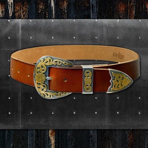 Puede incluir: Un cinturón de cuero marrón con una hebilla de plata y oro con un intrincado diseño floral. La hebilla está grabada con la palabra "Belts".