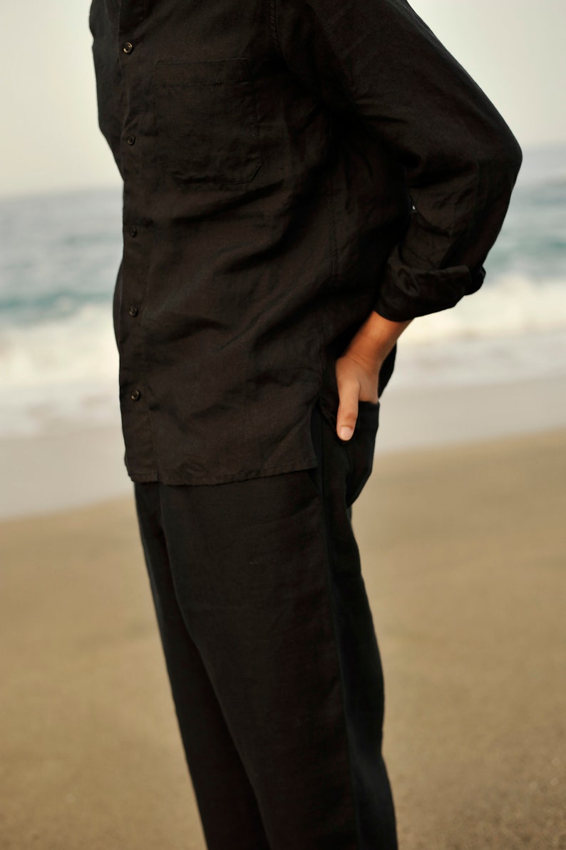 Pu&ograve; includere: Un completo in lino nero composto da una camicia e pantaloni. La camicia ha un colletto abbottonato e una tasca sul petto sinistro. I pantaloni hanno una gamba dritta.