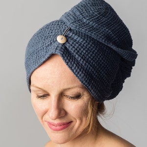 Peut inclure: Un turban de serviette à cheveux bleu avec une texture gaufrée et une fermeture à bouton en bois. Le turban est enroulé autour de la tête d'une personne, le bouton assurant la fermeture. Fond gris uni.