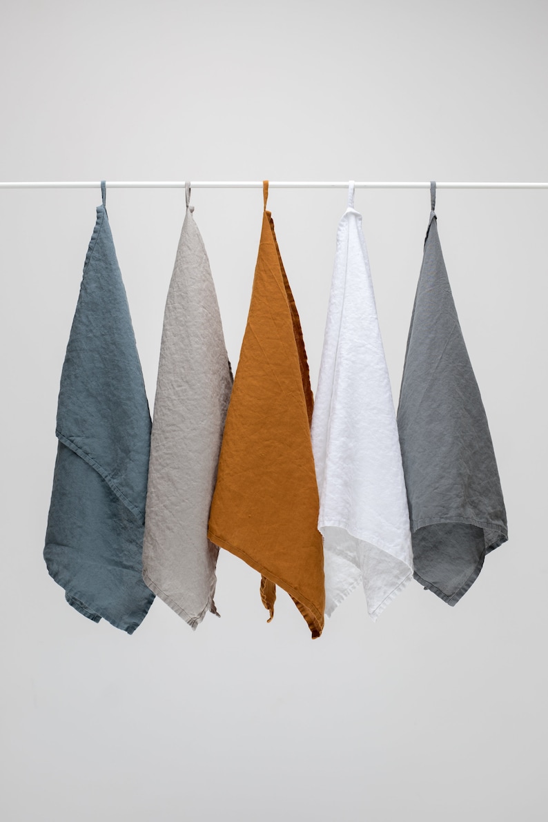 K&ouml;nnte beinhalten: F&uuml;nf Leinen-Geschirrt&uuml;cher h&auml;ngen an einer wei&szlig;en Stange. Die T&uuml;cher sind in den Farben Grau, Beige, Orange, Wei&szlig; und Dunkelgrau.