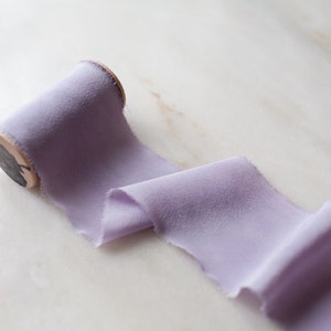 Handmade and hand dyed lilac silk chiffon ribbon with a hand frayed edge on a wooden spool.