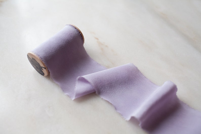 Handmade and hand dyed lilac silk chiffon ribbon with a hand frayed edge on a wooden spool.