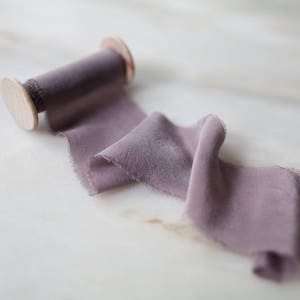 Handmade and hand dyed silk chiffon ribbon with a hand frayed edge on a wooden spool.