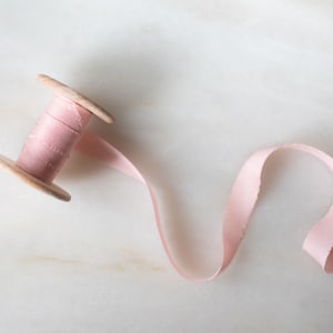 Handmade and hand dyed half inch narrow pink silk ribbon with a hand torn edge and available on a wooden spool.