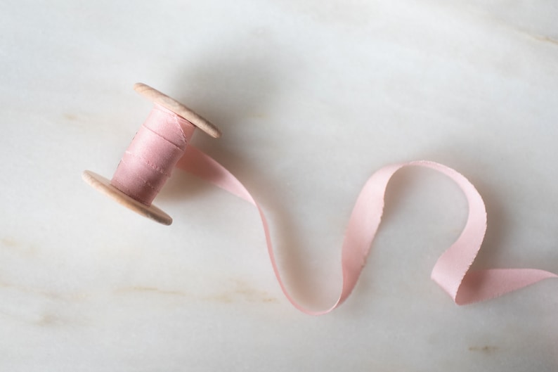 Handmade and hand dyed half inch narrow pink silk ribbon with a hand torn edge and available on a wooden spool.