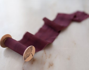 May include: A spool of deep burgundy silk ribbon with a wooden spool and a leaf design on the end.