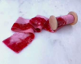 May include: A spool of pink and red velvet ribbon with a wooden spool. The ribbon is soft and has a subtle sheen.