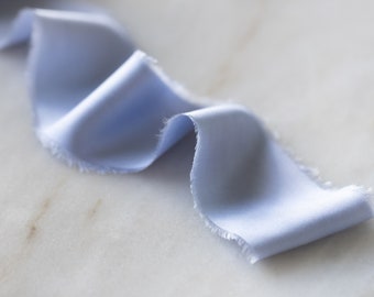 May include: A light blue satin ribbon with a frayed edge, lying on a white marble surface.