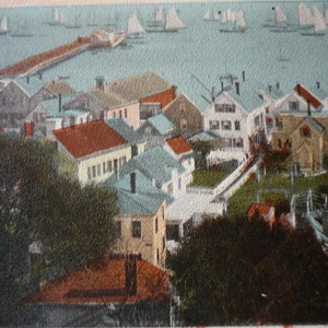 May include: A vintage postcard showing a coastal town with a pier stretching out into the water. The town is full of colourful houses and trees. Sailboats can be seen in the distance.