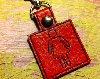 May include: Red leather keychain with a black outline of a female figure. The keychain has a silver metal clasp and a silver metal button.