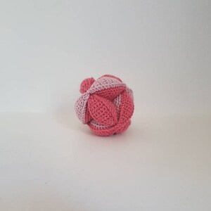 May include: A pink and light pink crocheted ball with a geometric pattern.