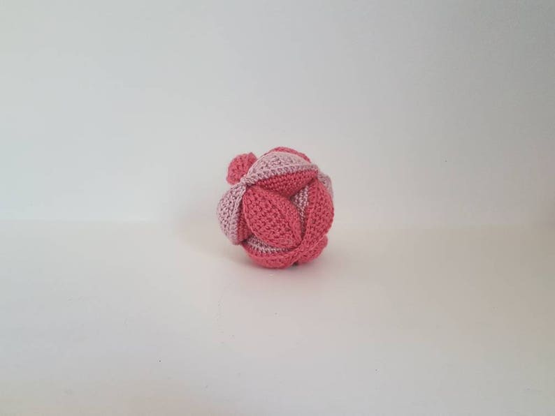 May include: A pink and light pink crocheted ball with a geometric pattern.