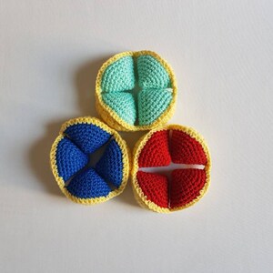 May include: Three crocheted balls with yellow trim. The balls are divided into four sections each. The sections are blue, red, and light blue.