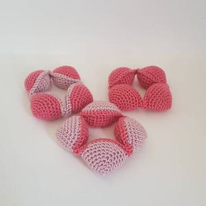May include: Three crocheted toys made of pink and white yarn. The toys are shaped like balls and are connected together to form a chain.