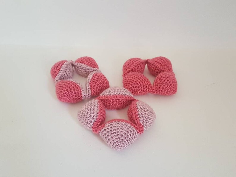 May include: Three crocheted toys made of pink and white yarn. The toys are shaped like balls and are connected together to form a chain.