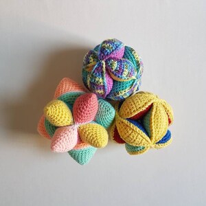 May include: Three crocheted balls in different colors and patterns. The balls are made of yarn in shades of pink, yellow, green, blue, and red. The balls are arranged in a triangular shape.