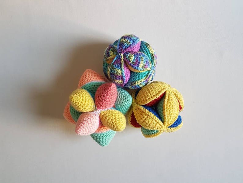 May include: Three crocheted balls in different colors and patterns. The balls are made of yarn in shades of pink, yellow, green, blue, and red. The balls are arranged in a triangular shape.