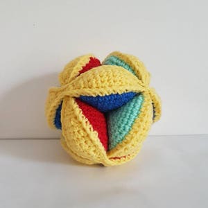 May include: A yellow, blue, red, and green crocheted ball toy. The ball is made of multiple pieces that are sewn together.