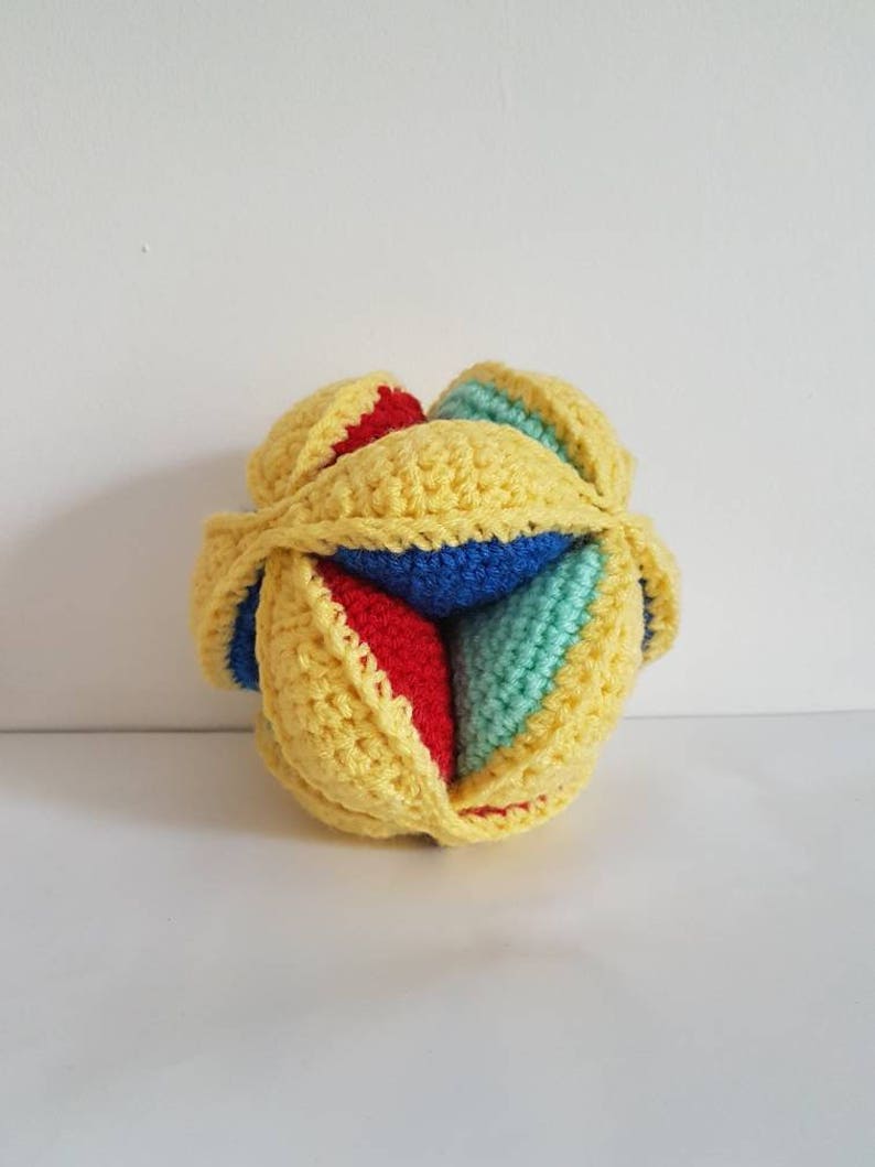May include: A yellow, blue, red, and green crocheted ball toy. The ball is made of multiple pieces that are sewn together.