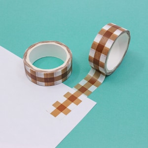 May include: Two rolls of brown and white checkered washi tape. One roll is unwinding and the tape is laying on a white surface.