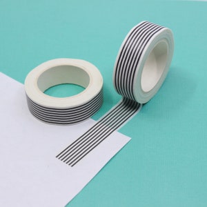 May include: Two rolls of black and white striped washi tape. The tape is unrolled on a white surface with a turquoise background.