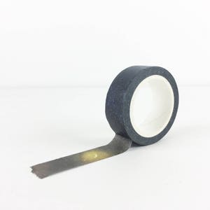Puede incluir: Un rollo de cinta washi negra con un estampado de galaxia que presenta una luna creciente y estrellas. La cinta est&aacute; parcialmente desenrollada, revelando el dise&ntilde;o.