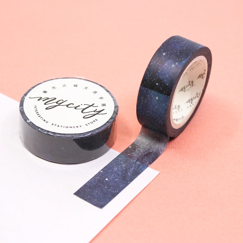 Puede incluir: Un rollo de cinta washi negra y azul con un estampado de galaxia. La cinta est&aacute; etiquetada "mycity interesting stationery store" en texto blanco.