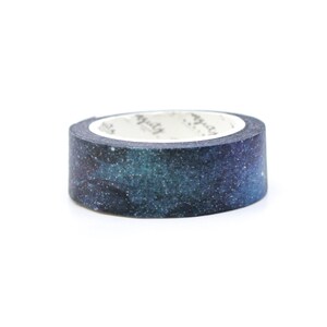 Puede incluir: Un rollo de cinta washi con estampado de galaxia. La cinta es azul y negra con purpurina blanca. La cinta est&aacute; sobre un fondo blanco.