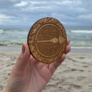 Puede incluir: Un posavasos de madera con un dise&ntilde;o circular que presenta una flecha estilizada que apunta hacia la derecha. El posavasos tiene un acabado de madera de grano marr&oacute;n y est&aacute; rodeado por un c&iacute;rculo de detalles intrincados.