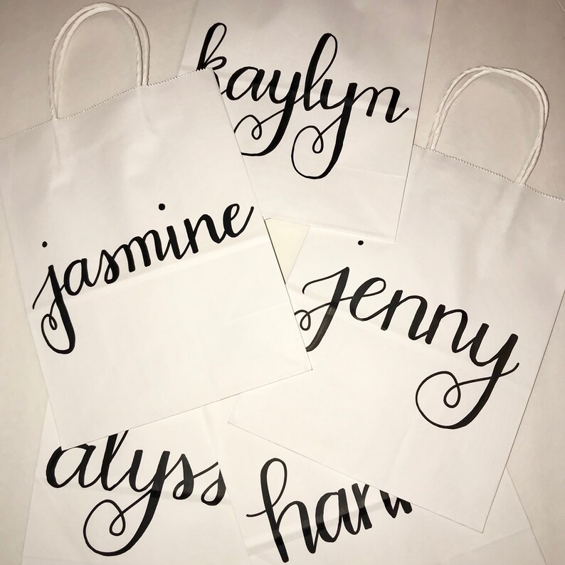 May include: White paper gift bags with twisted paper handles. Each bag features a name in elegant black calligraphy: Jasmine, Kaylyn, Jenny, Alyss, and a partial name. Ideal for personalized gifts or event favors.