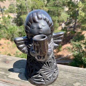 May include: Black ceramic angel figurine with intricate carved details. The angel is holding a small vase or cup in its hands.
