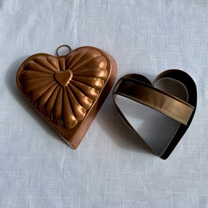 May include: Two heart-shaped baking molds. One is a copper mold with a fluted design and a small heart in the center. The other is a metal cookie cutter.