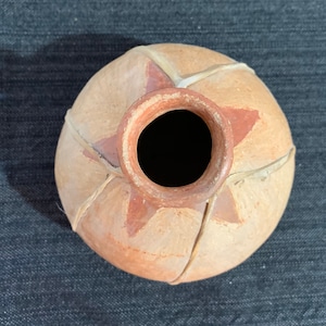 May include: A round, terracotta pottery vase with a star design and a light brown glaze. The vase is decorated with a woven pattern of light brown strips.