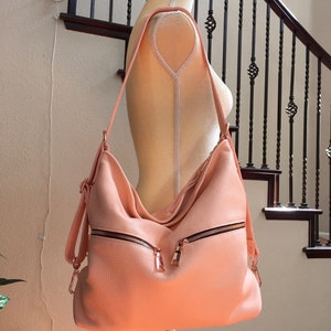 May include: A blush pink leather shoulder bag with gold-toned hardware and zipper accents. The bag has a flap closure and a long adjustable strap.